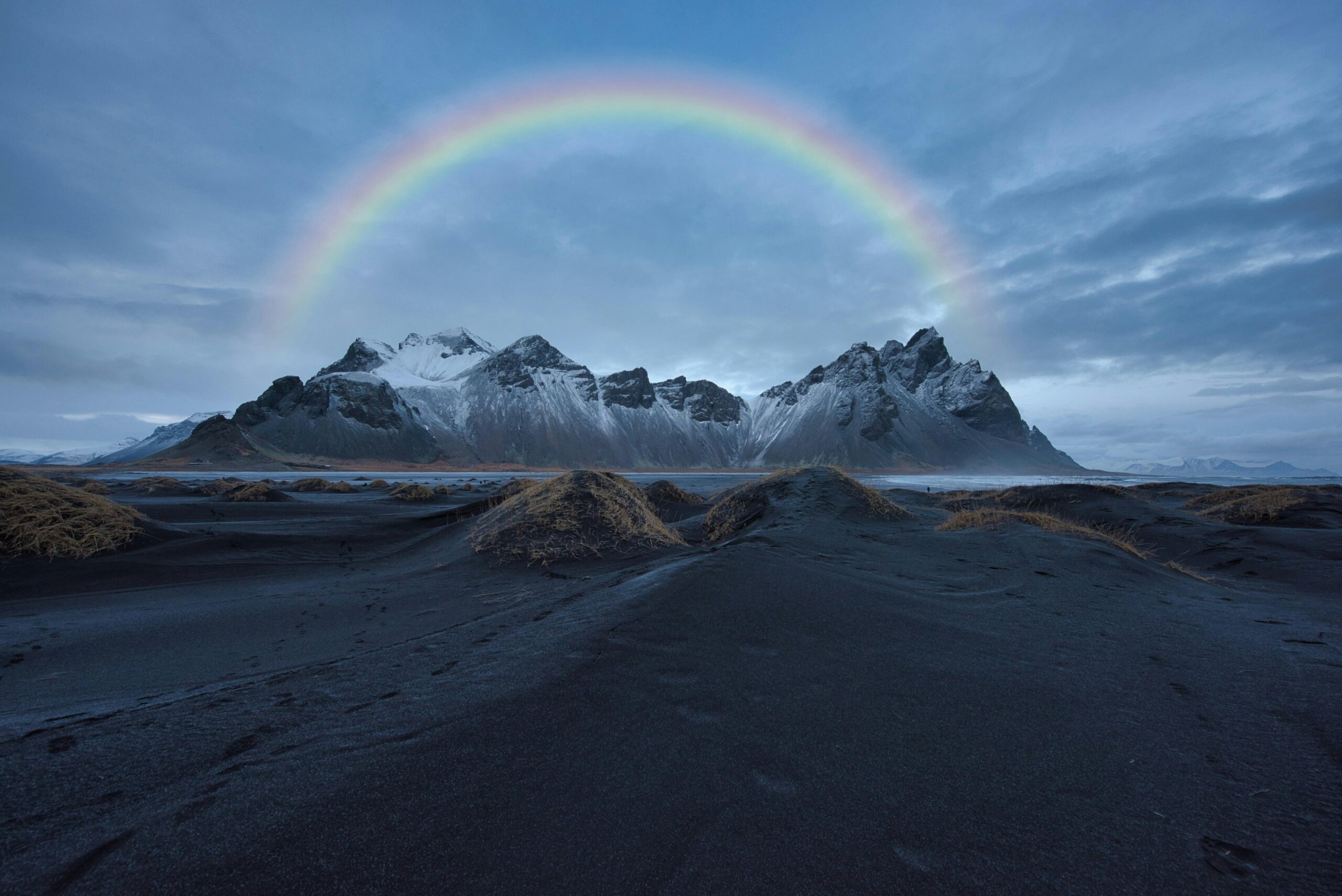 Stunning view of Vestrahorn mountain with a vibrant rainbow arching over the black sand beach in Iceland.